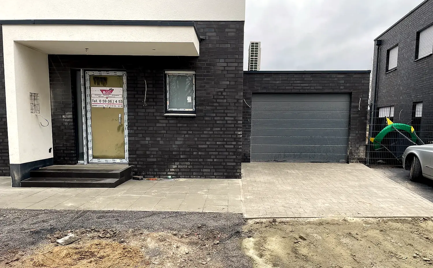 Gepflasterte Garagenzufahrt und Eingang an einem modernen Neubau