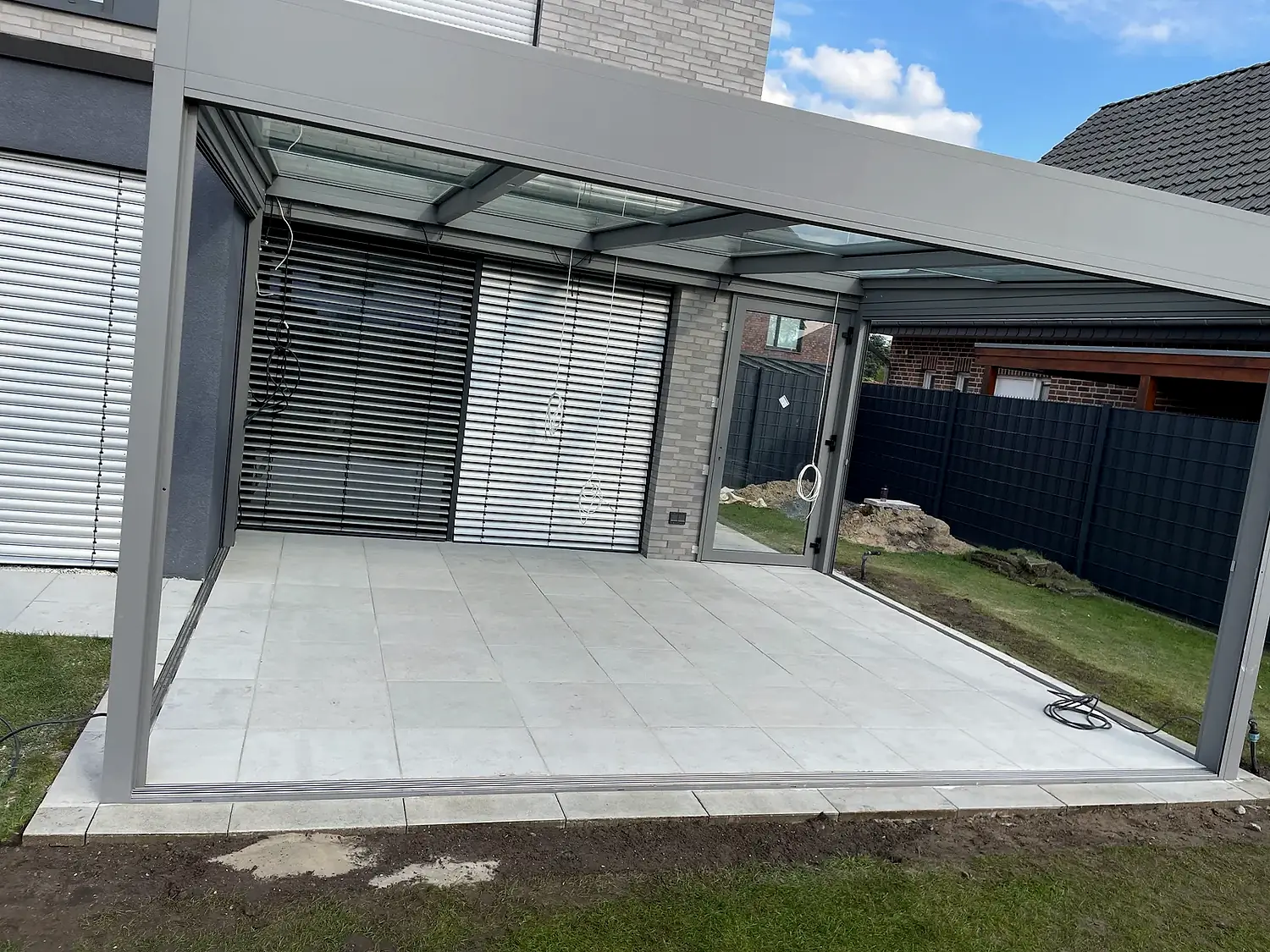 Überdachte Terrasse mit hellem Plattenbelag und angrenzendem Rasen